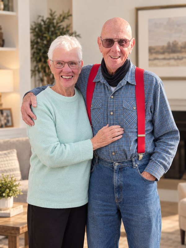 An older couple standing arm in arm and smiling in their living room